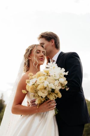 A romantic wedding portrait featuring a stunning white bouquet against an overcast sky.