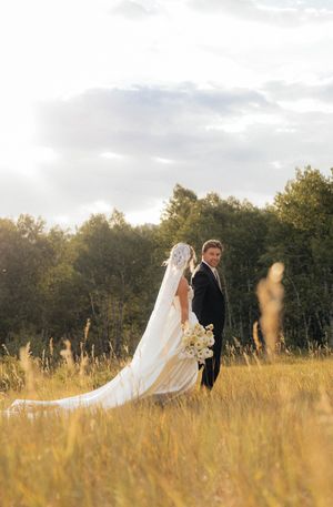 A sunset wedding portrait of a couple standing in a golden field with flowing veil.