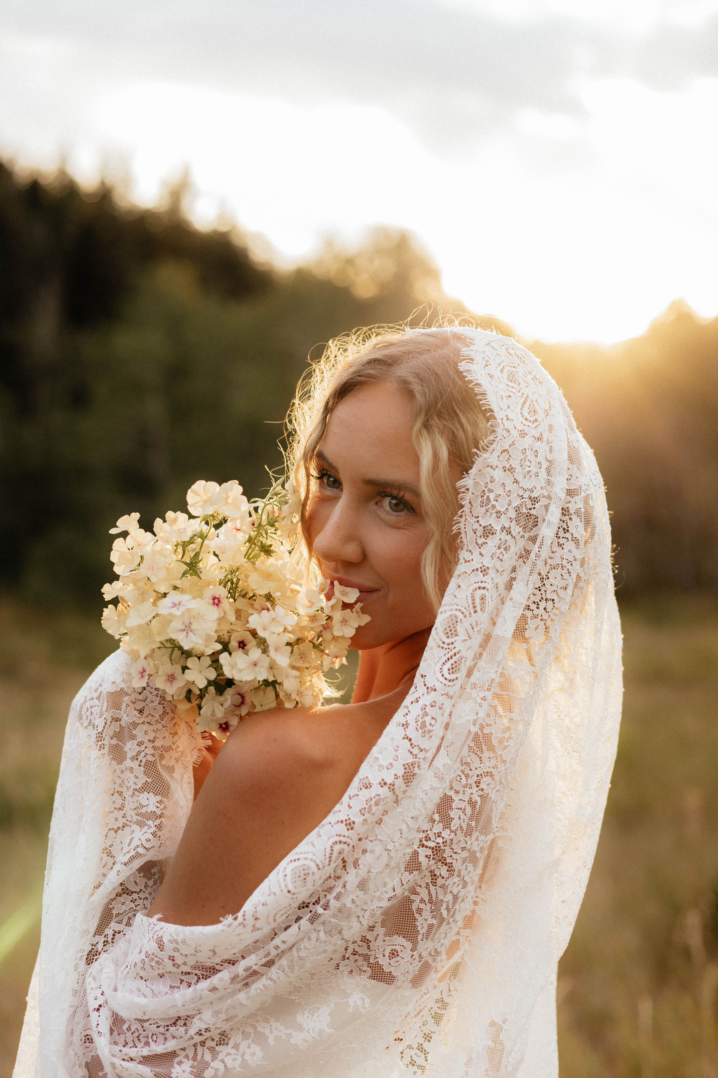 A radiant bridal portrait with sunlit lace veil and white bouquet.
