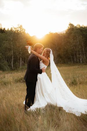 A romantic sunset embrace in a field with flowing white wedding dress and veil.