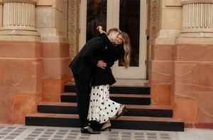Stylish couple flirts and dances near classic architectural columns.