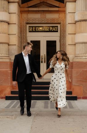 Couple in formal wear plays and dances outside Exchange Place building entrance.