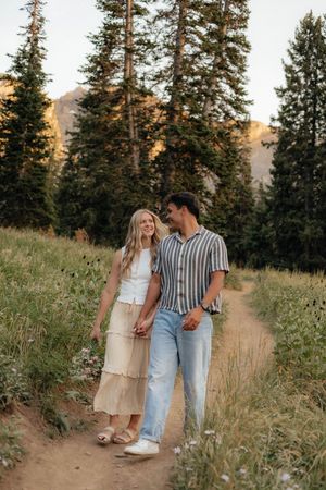 A couple strolls along a dirt path through mountain wildflowers at sunset.