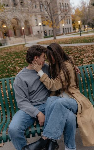 Two people share an intimate moment on a park bench surrounded by fallen autumn leaves.