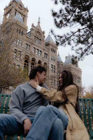 A couple embraces on a bench with a Gothic-style building visible in the background.
