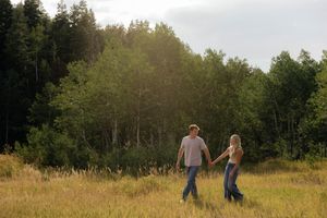 A couple enjoys a peaceful moment in a sunny meadow surrounded by forest.