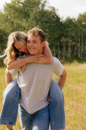 A playful piggyback ride moment in a sunny field with trees in the background.
