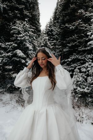 Ethereal bridal portraits in the snow with a flowing white ballgown among snow-covered trees.