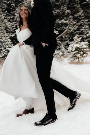 Wedding couple's feet and dress hem in snow, showing formal shoes against white winter ground.