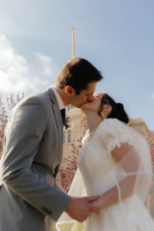 A romantic wedding kiss in front of a church with cherry blossoms blooming.