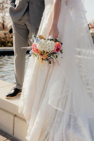 A close-up of a bridal bouquet with pink and white flowers against a flowing wedding dress.