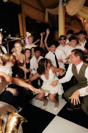 Energetic wedding reception dance floor with bride, groom, and guests celebrating together on a black and white checkered floor.