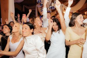 Joyful group of women in white and pastel dresses celebrating and cheering together at a lively wedding reception.
