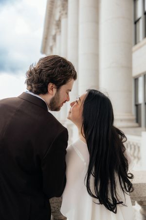 A couple embracing affectionately in front of a building with classical architectural columns.