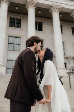 A couple embracing and kissing in front of a grand, columned building.