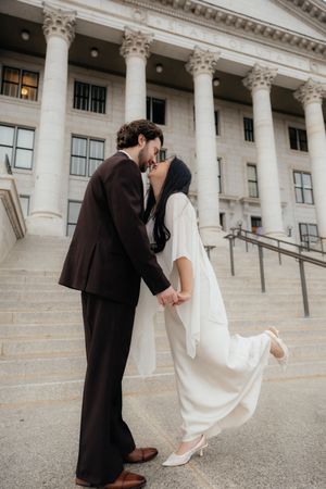 A couple embracing and kissing in front of a grand, columned building.