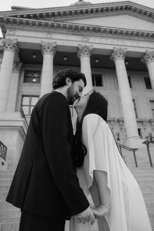 A black and white image of a couple embracing in front of a grand, columned building.
