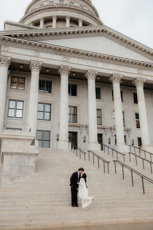A bride and groom stand on the steps of a grand, columned building.