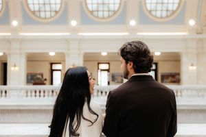 A couple walking together in an elegant indoor setting with a mural in the background.