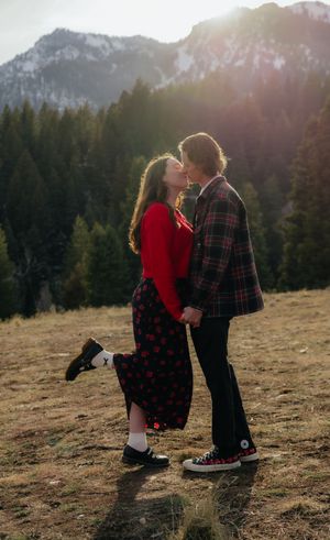 A couple embracing in a scenic mountain landscape with a forest in the background.