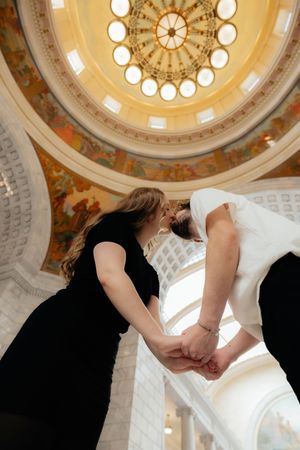 Two women holding hands in an ornate, domed interior with intricate architectural details.