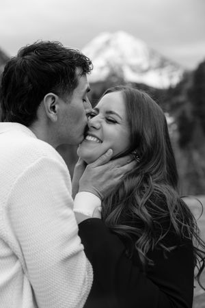 A black and white image showing a loving couple embracing and smiling affectionately in a scenic outdoor setting.