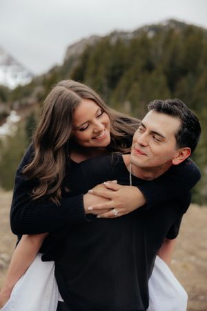 A young couple embracing outdoors against a backdrop of mountains and trees.