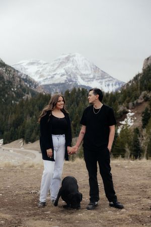 A couple walking together with a dog in a scenic mountain landscape.