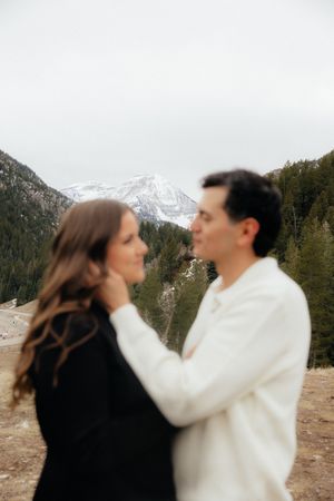 A couple embracing in a scenic mountain landscape with snow-capped peaks in the background.