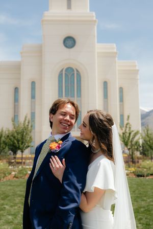 Bride and groom posing in front of a white LDS temple on their wedding day, mountains visible in background.