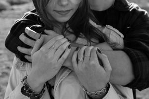 Black and white photo of a couple embracing, showing intertwined hands with rings and bracelets.