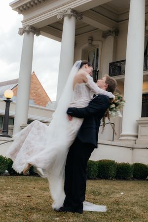 A bride and groom embrace in front of a grand, columned building on their wedding day.