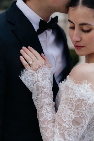 A close-up of a bride and groom embracing tenderly, with the bride's lace-detailed dress and the groom's tuxedo visible.