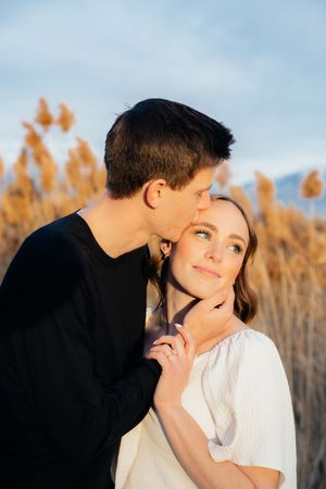 A young couple embracing affectionately in a field of tall grass against a cloudy sky.