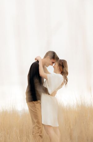 A couple embracing in a field of tall grass, with a soft, warm light surrounding them.
