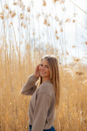 A smiling woman standing in a field of tall, golden grass.