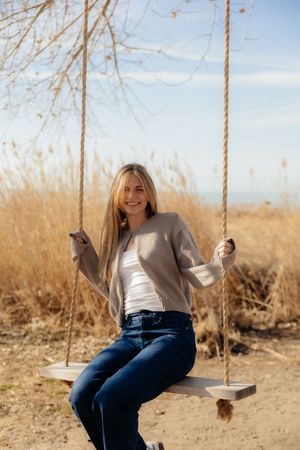 A smiling young woman sitting on a swing in a field on a sunny day.