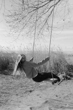 A black and white image of a woman swinging on a swing in a natural environment.