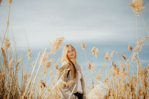 A woman stands in a field of tall golden grass, smiling and enjoying the outdoors.
