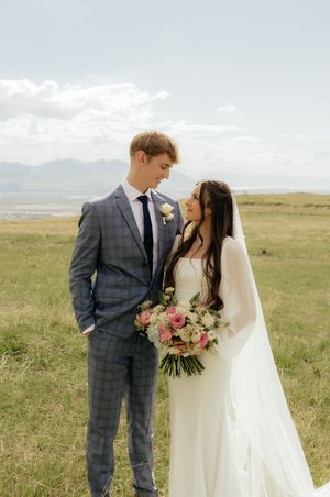 A bride and groom share a romantic moment in an open field with mountain views on their wedding day.
