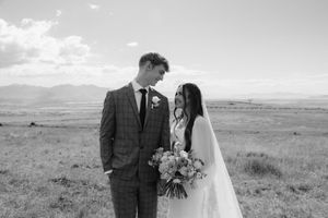 Black and white photo of a bride and groom sharing a romantic moment in an open field with mountains in the background.