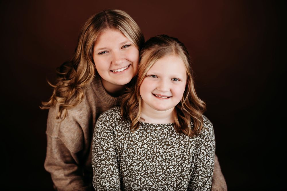 Two young girls in matching outfits smiling against dark background.