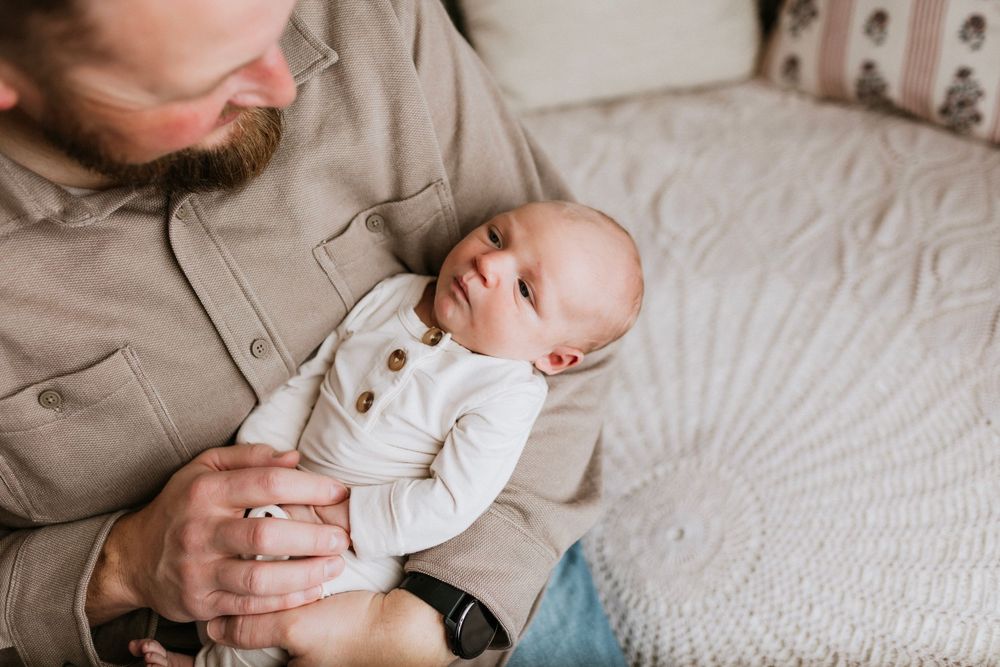 Tender black and white photo series showing gentle moments between parent and newborn baby on white bedding.