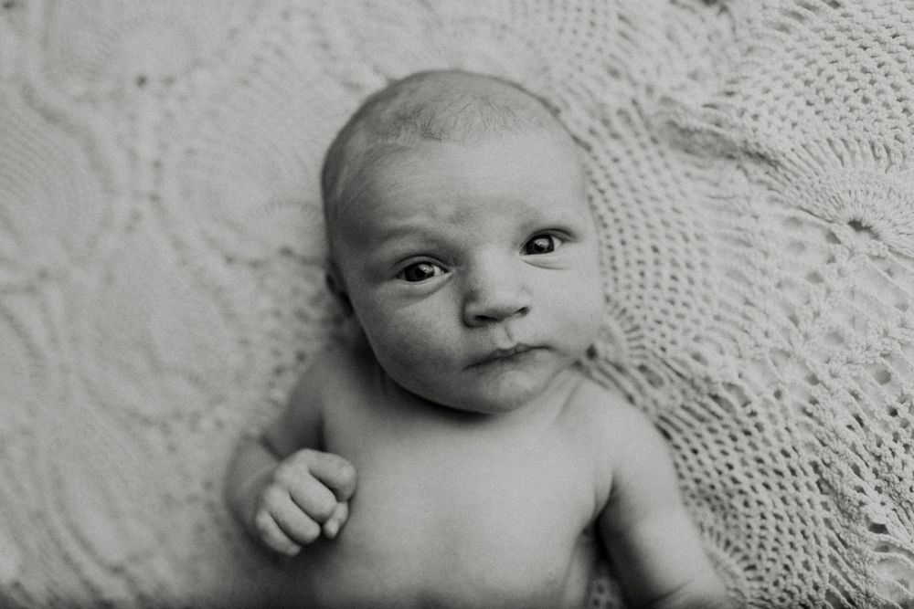 Black and white series showing a newborn baby with various expressions while lying on lace fabric.