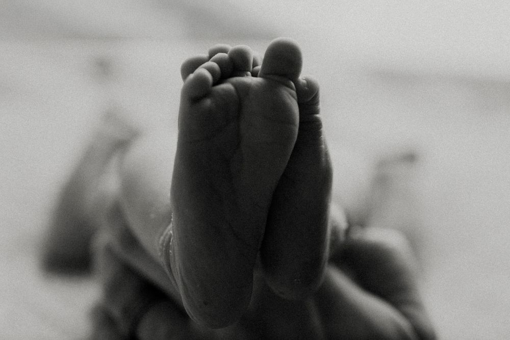 Series of intimate monochrome photographs capturing parent cradling newborn baby against neutral background.