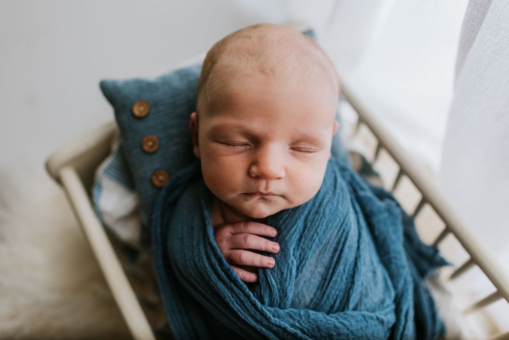 Newborn baby wrapped in soft teal swaddle blanket during professional photo session.