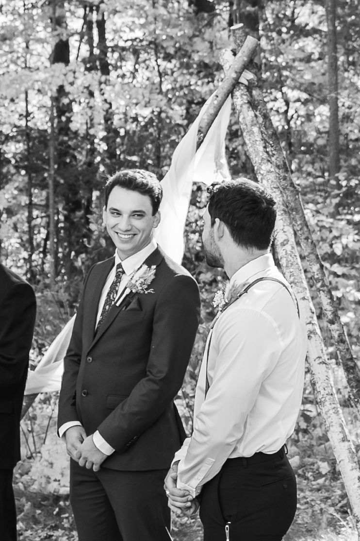 Black and white photo of a joyful wedding ceremony moment in a forest setting with two people in formal attire.