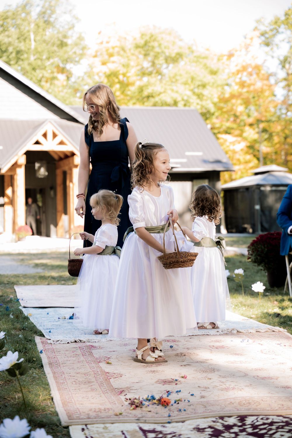 Young attendants in white dresses scatter flower petals along a path during a wedding ceremony.