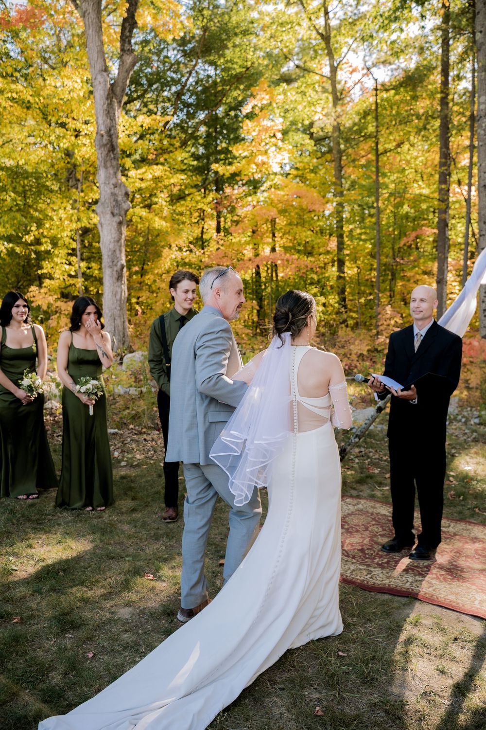 Wedding party poses together on a wooded path surrounded by vibrant autumn foliage on a sunny afternoon.