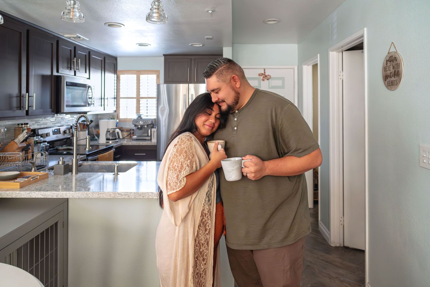 Mom leaning cozily up to dad while drinking a cup of coffee in the kitchen. In-home family session.  Doughman Photography